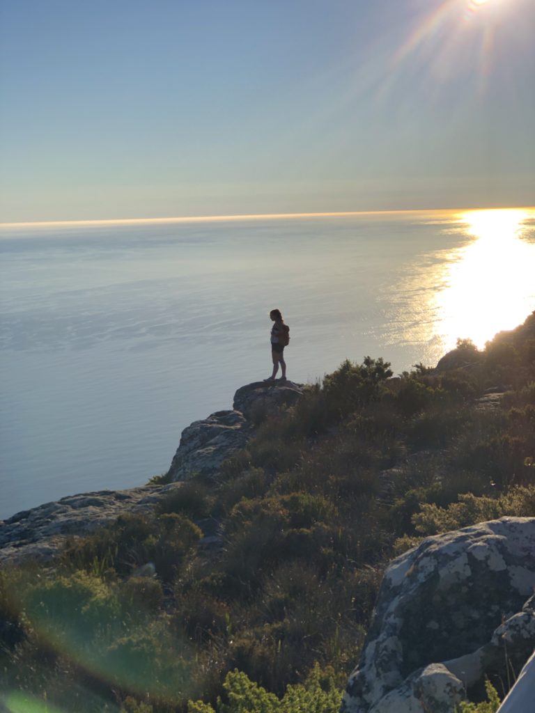 woman standing on edge of Table Mountain in Cape Town with sunset behind her