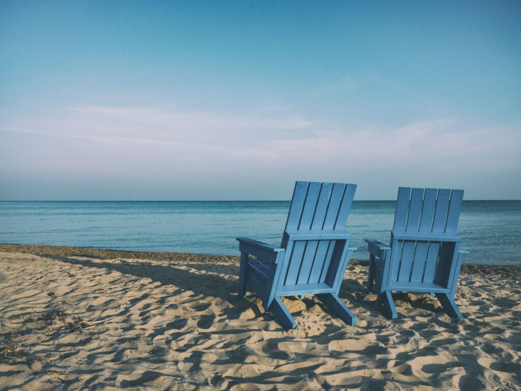 two blue Adirondack chairs on the beach