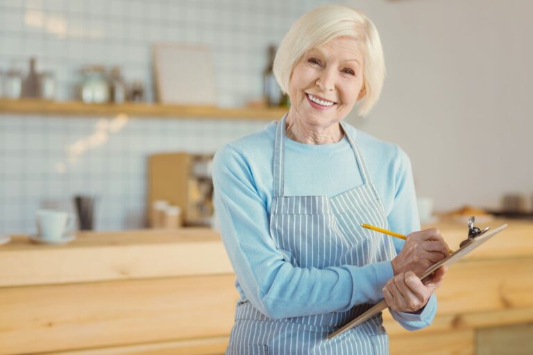 older woman smiling at the camera and holding a clipboard and pencil