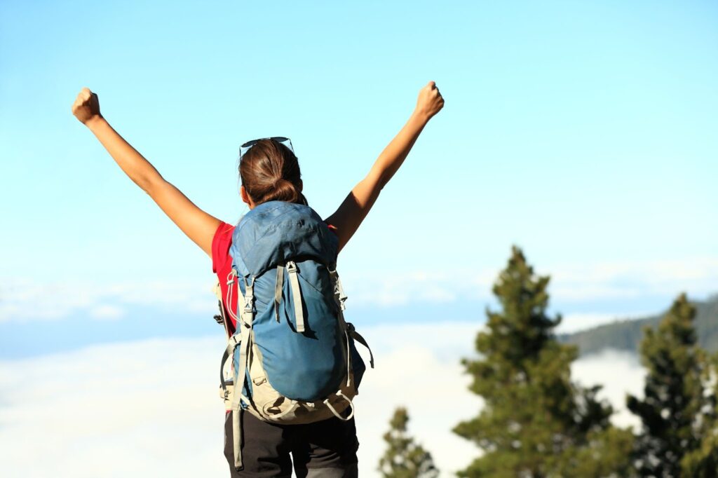 woman wearing a backpack standing on top of a mountain, arms in the air in a victory pose