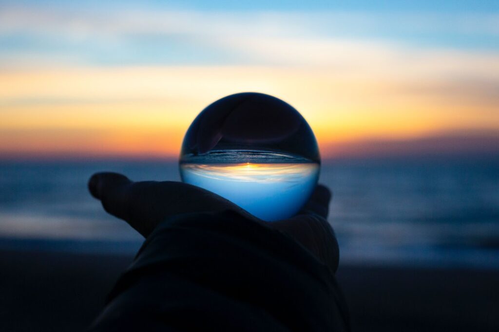 silhouette of a hand holding a glass ball that's reflecting the ocean and sky at dusk. ocean in the background out of focus