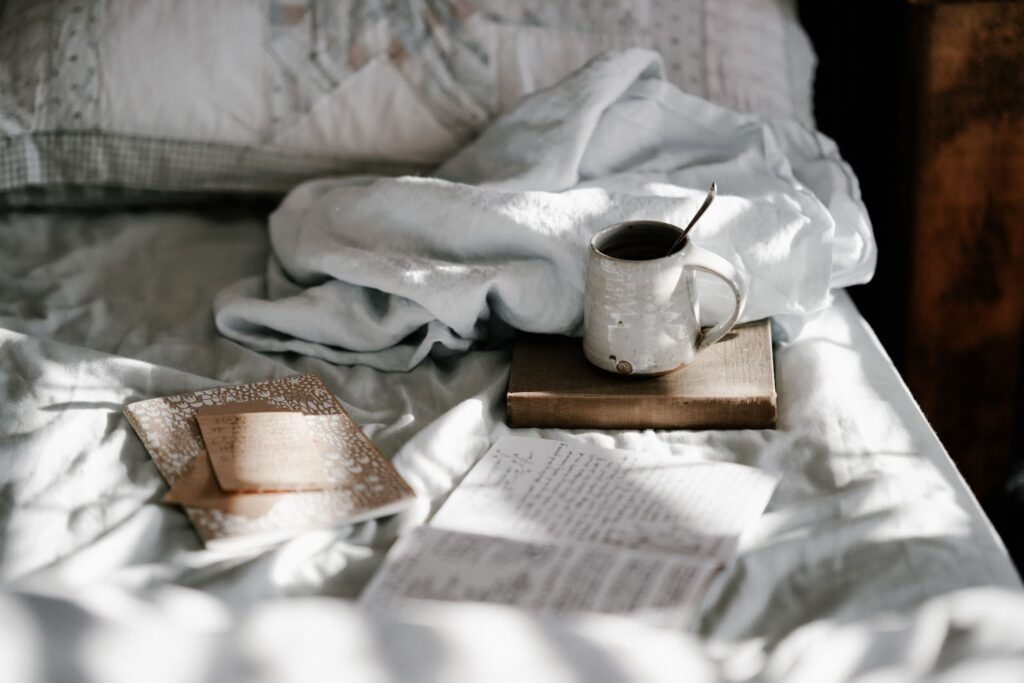 items on a bed: open journal, notebook, book with coffee mug sitting on it