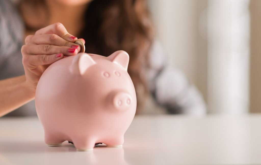 woman putting a coin in a pink piggy bank