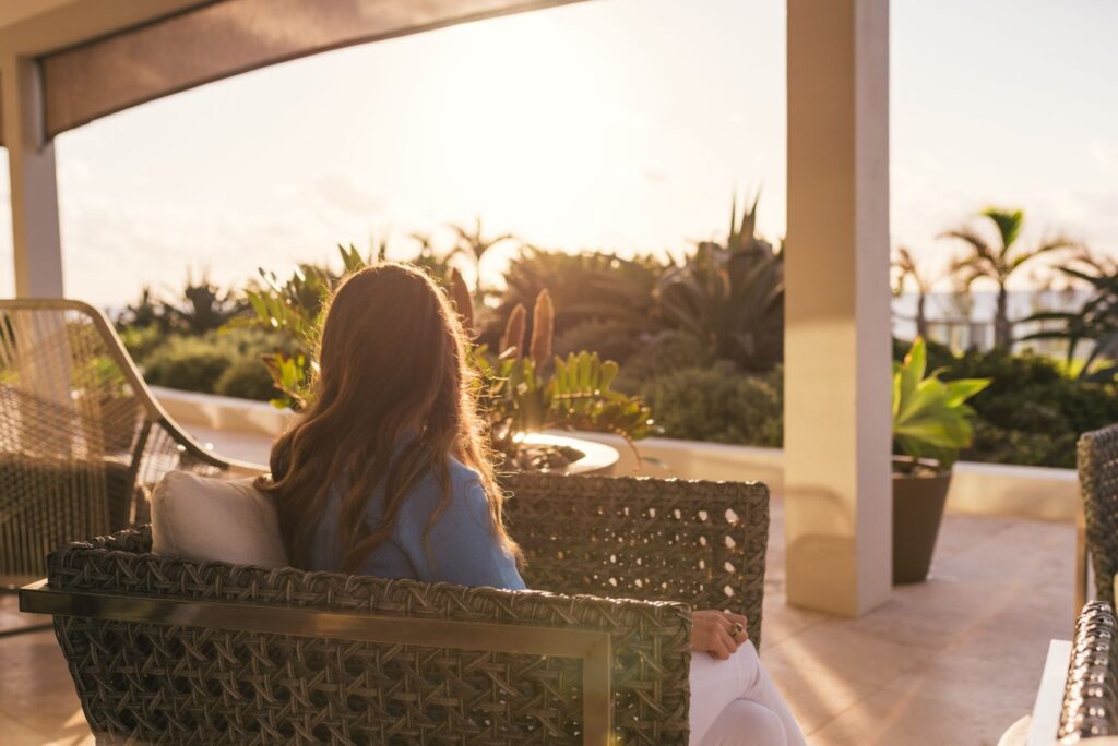 woman sitting on a rattan chair on a patio. Ocean and palms in the background