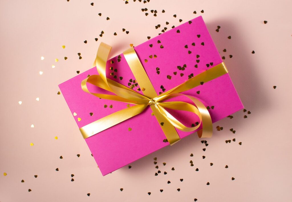 gift wrapped in pink paper with gold bow. Heart-shaped confetti scattered on and around the gift