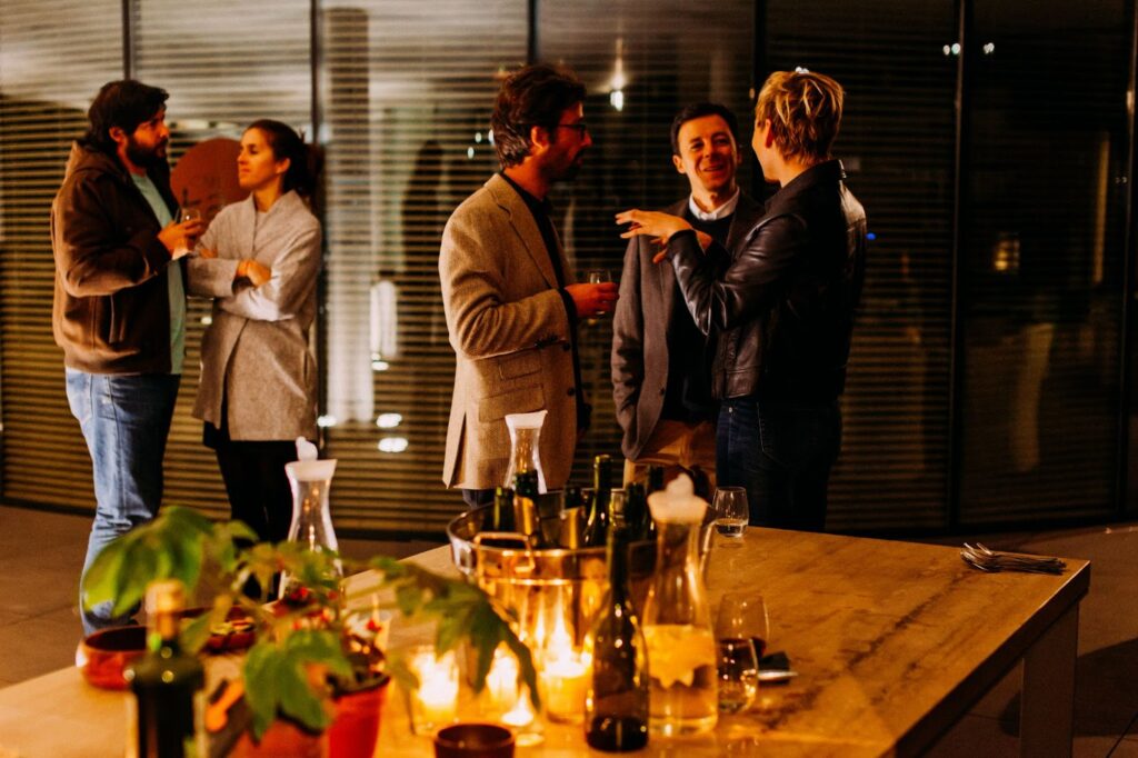 two groups of people chatting at a cocktail party. Table with drinks and glasses in the foreground. Offices in the background