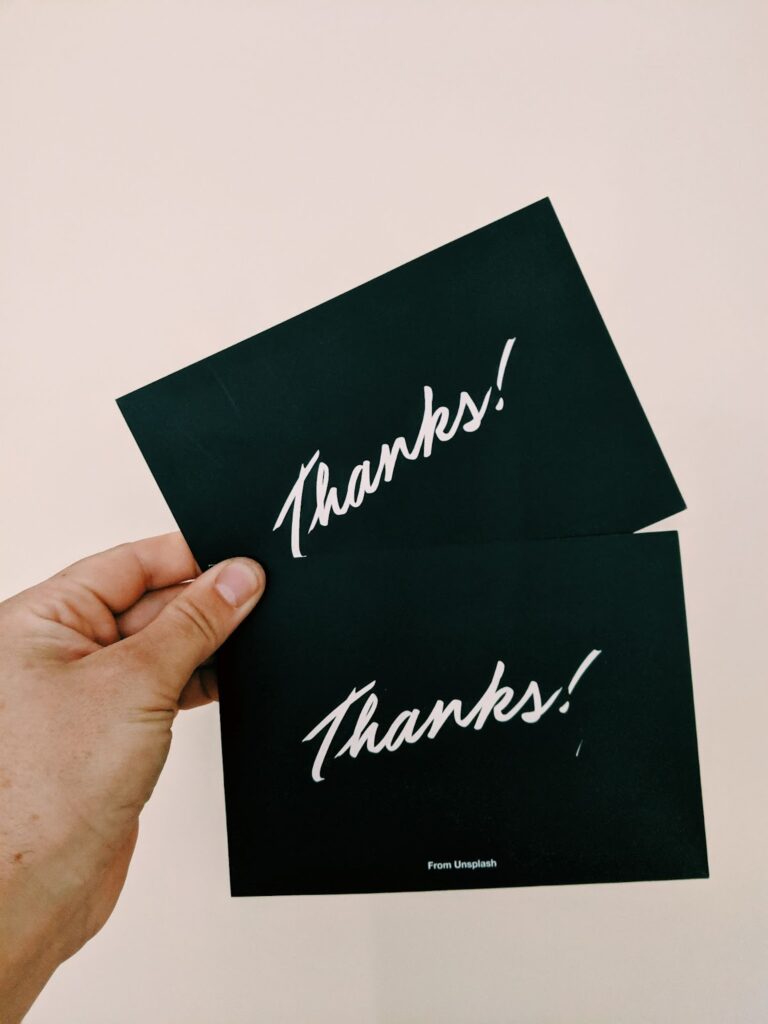 hand holding two black cards with white writing. Text on cards: "Thanks!"