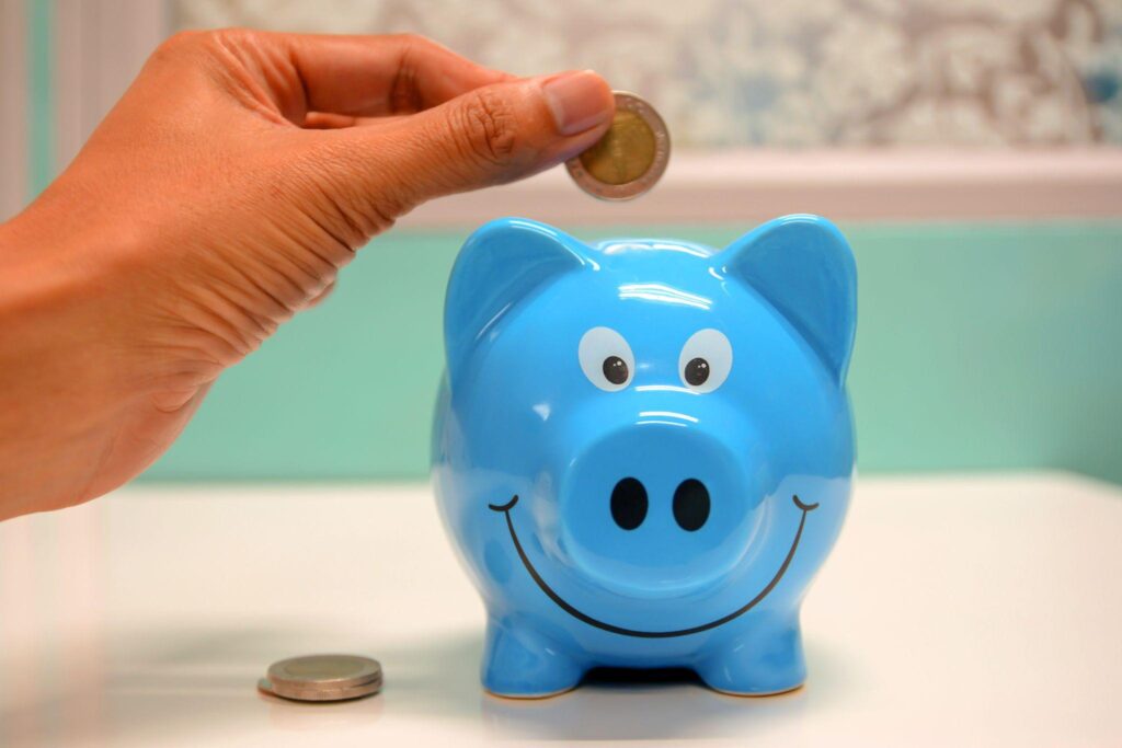 person putting a coin into a blue piggy bank