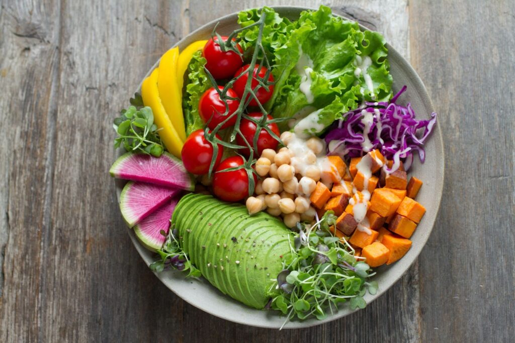 bowl of cut vegetables and fruits, including avocado, sprouts, sweet potato, cabbage, lettuce, cherry tomatoes, yellow bell pepper, and dragon fruit