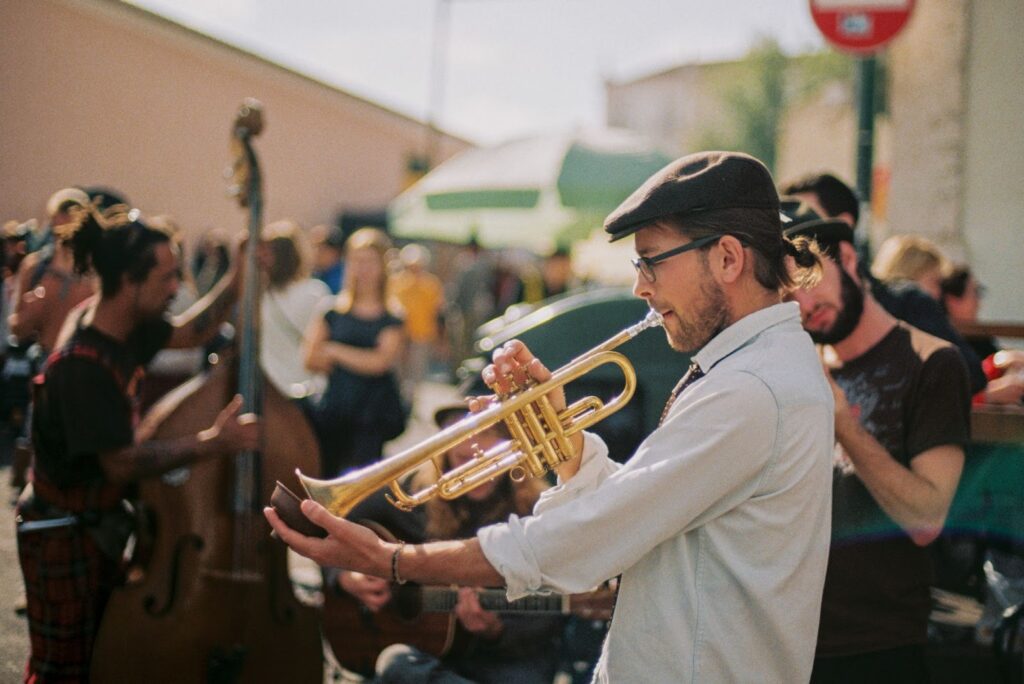 man playing a trumpet in the foreground; other band members, street festival scene in the background