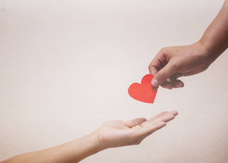 one hand holding a red paper heart, putting it into another hand