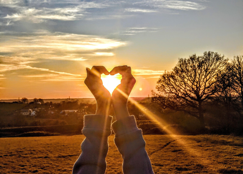 two nands forming the shape of a heart around a sunset