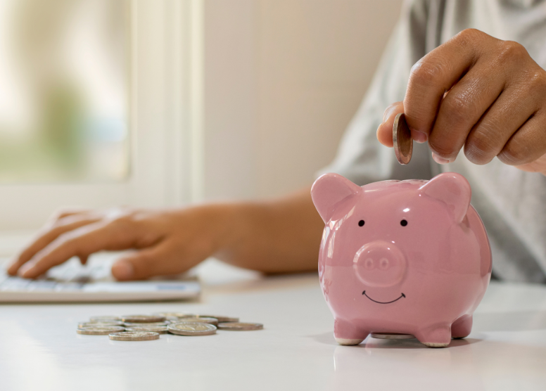 person dropping coins in a pink piggy bank