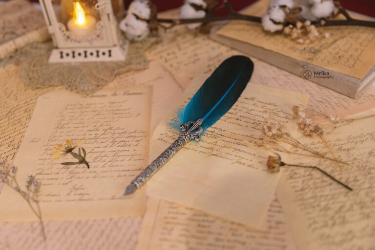 fountain pen with blue feather top resting on handwritten pages. Dried flowers, cottonwood branch, and candle around pen