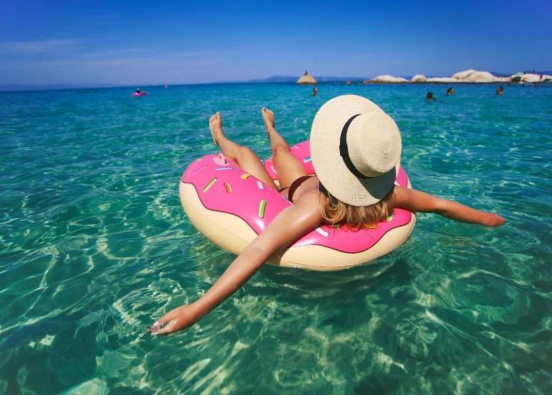 woman floating in the ocean on an inner tube that looks like a donut with pink frosting and sprinkles