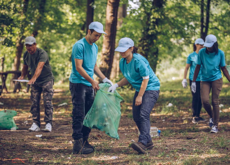 group of people in matching teal tshirts picking up trash in a wooded area