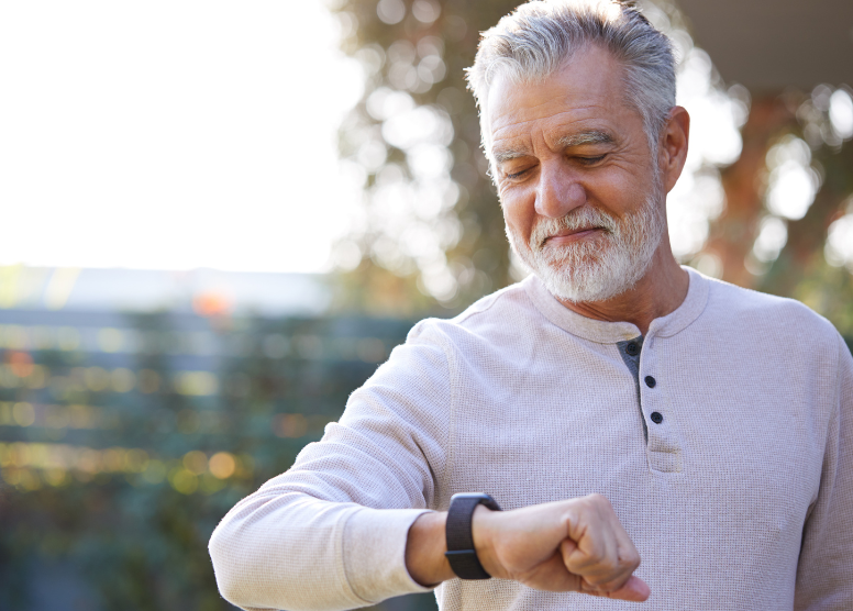 Man with gray hair standing outdoors looking at his smartwatch on his wrist