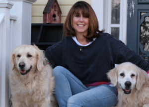 Janice sitting on the front porch of her house with her two golden retrievers, Bailey and Joey