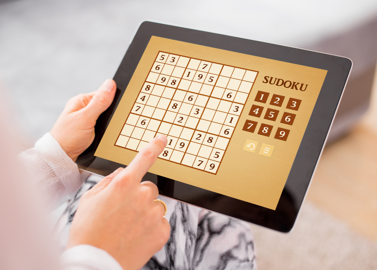 person holding a tablet computer with a sudoku game on the screen