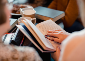 closeup of woman reading a book (holding a pair of glasses in the hand that she's holding the book open with)