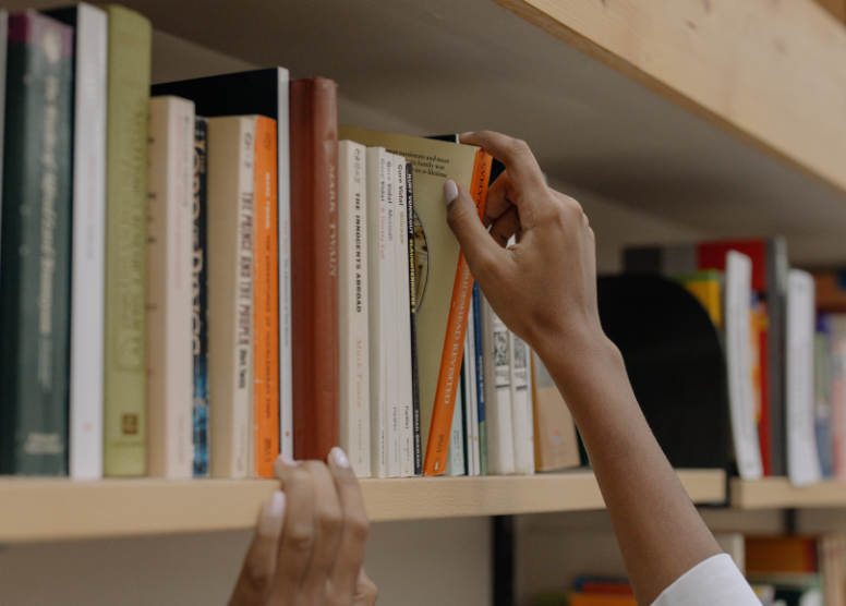 closeup of a woman's hands pulling a book down from a bookshelf in a bookstore or library