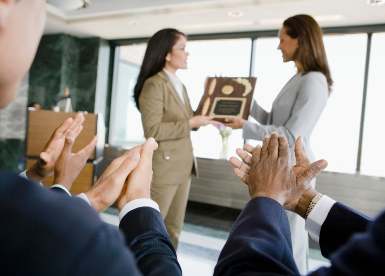 woman presenting a plaque to another woman. People applauding