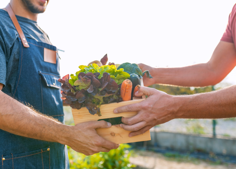 cropped image of a man on the right receiving a wooden crate full of vegetables from a farmer on the left