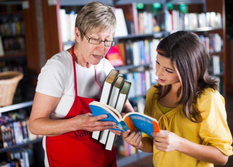 librarian holding several books helping a young woman with another book