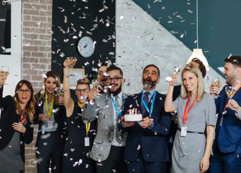 group of coworkers in an office celebrating with a cake, champagne, confetti