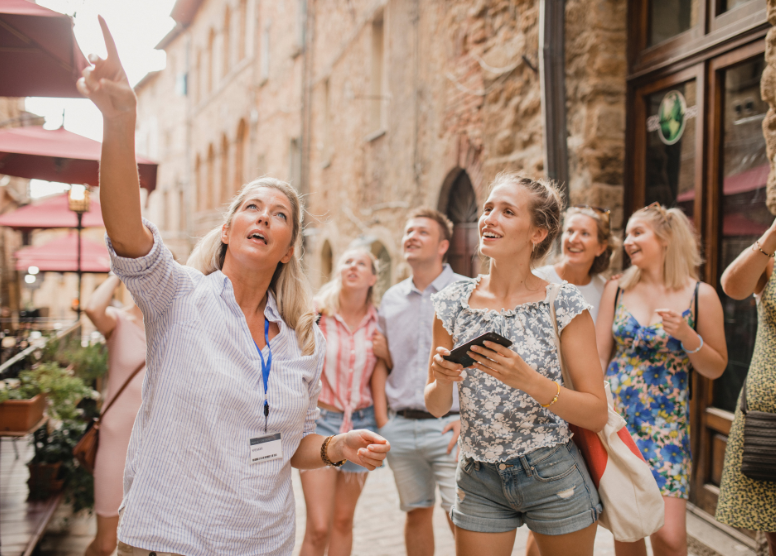 female tour guide leading a tour in a city. guide is pointing up and talking; tour participants looking up where she's pointing