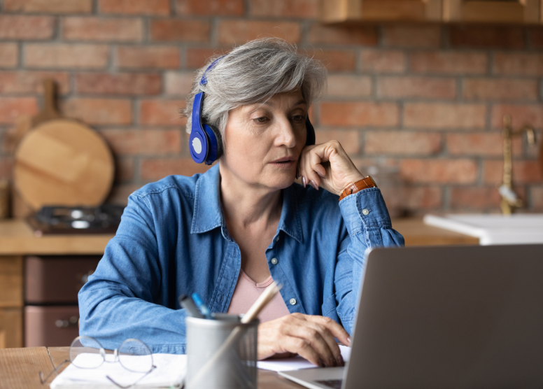 older woman wearing blue headphones sitting in front of a laptop