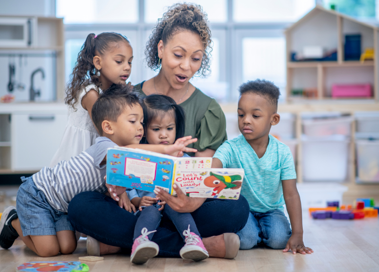 woman teacher sitting on the floor reading to toddlers