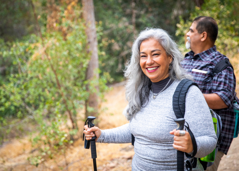 older man and woman hiking. woman is holding walking sticks