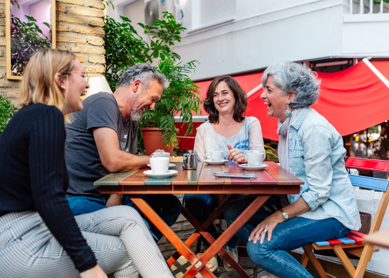 group of people sitting at a table outdoors, having coffee and laughing together