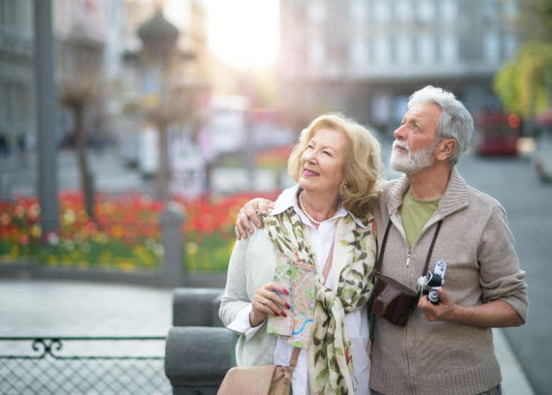 older man and woman sightseeing. both are looking up at something; man is holding a camera and woman is holding a map