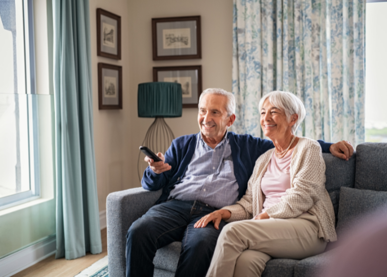 retired couple sitting on a couch watching tv