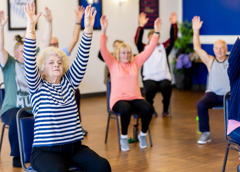 group of seniors doing seated exercises, sitting in chairs with their arms raised