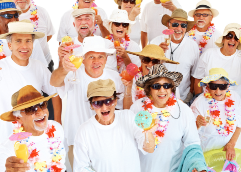 group of smiling senior citizens wearing fun hats and leis and holding up tropical drinks