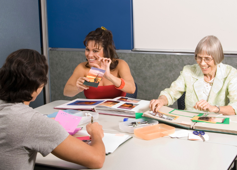 elderly woman and two younger adults creating scrapbooks together