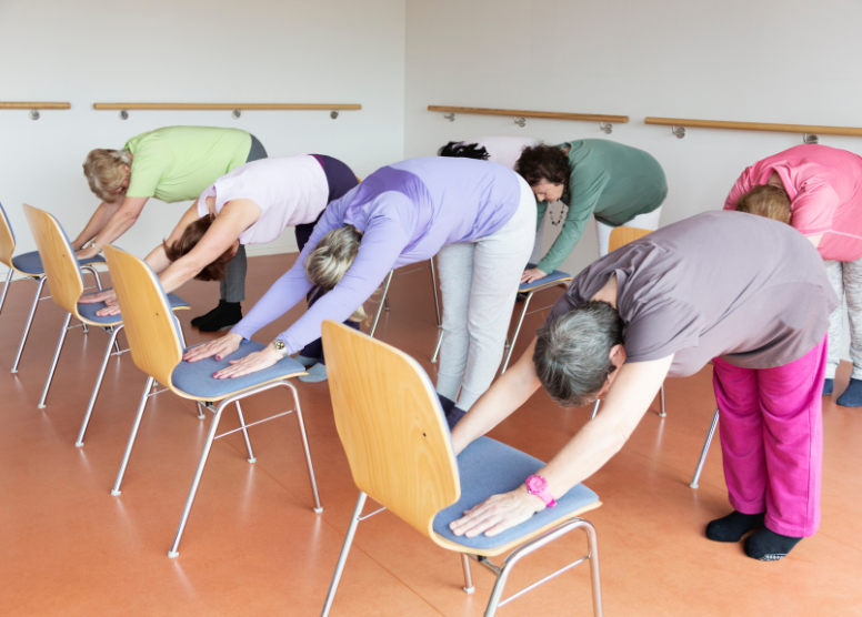 group of seniors stretching by leaning forward with hands on the seats of their chairs