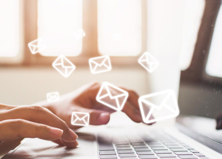 close up of hands typing on a laptop keyboard. Email envelope icons overlaid on image