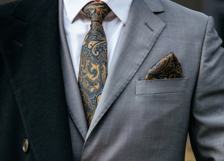 close up of man wearing gray business suit with black and gold paisley tie and pocket square