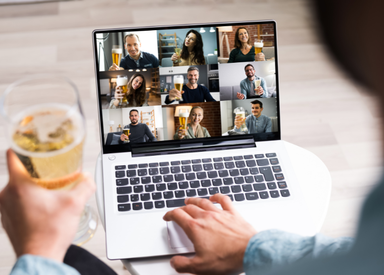 over-the-shoulder perspective of person making a toast with a group of people on a conference call on a laptop