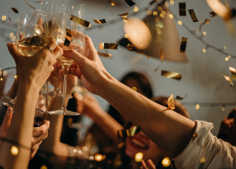 hands holding wine glasses up in a toast, with gold confetti falling around